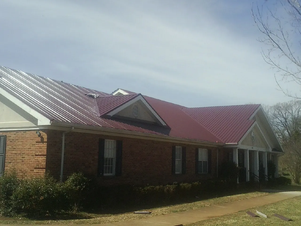 Red metal roof with gabled entries on a long brick building, from a Hail Damage Roof Repair job in Appleton