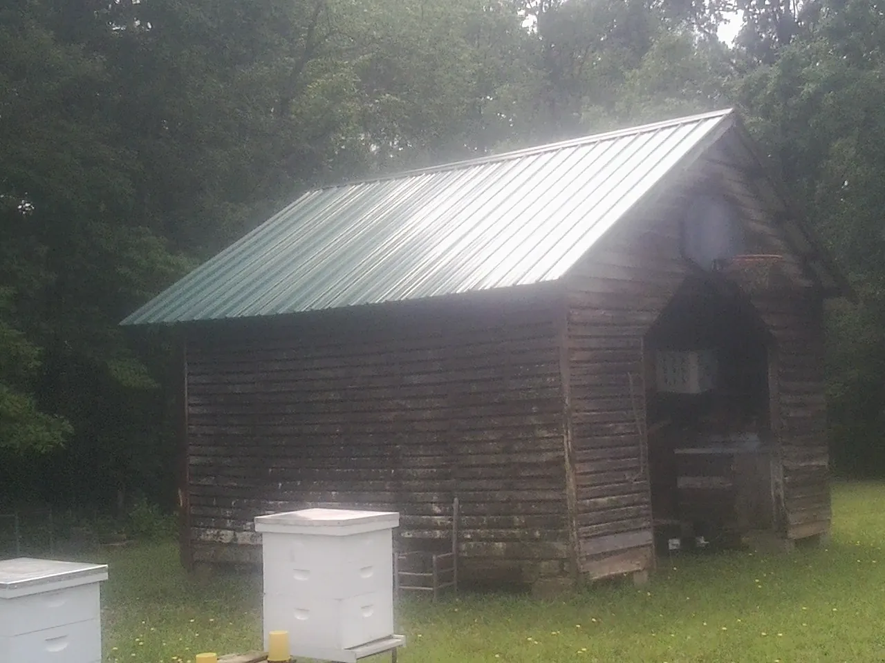 Green metal roof on a weathered barn beside stacked beehives in Appleton
