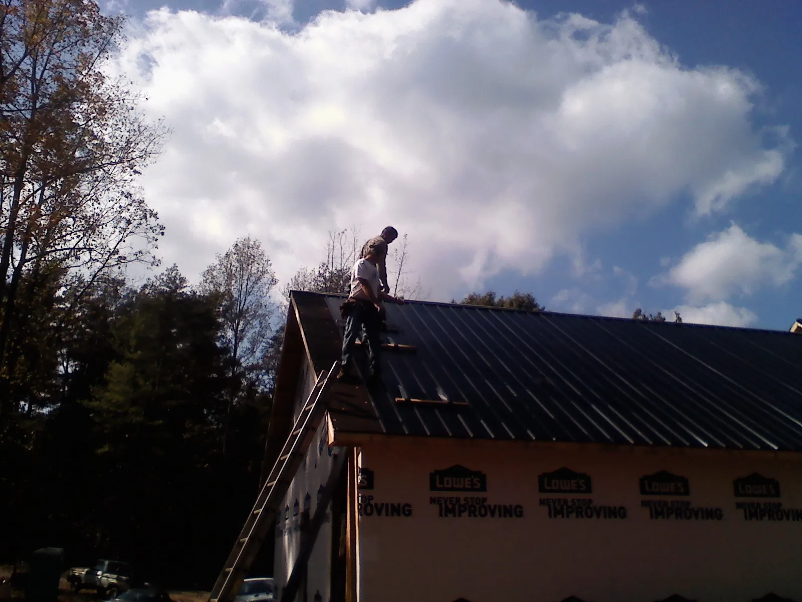 Roofer fastening dark metal panels high against a cloudy sky, from a Roof Inspection job in Appleton